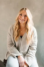 Stylish woman in jeans and sweater sitting at Salon M + Suites.