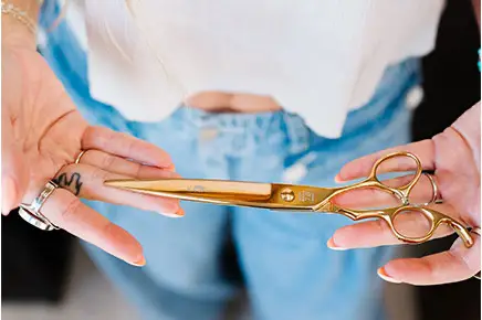 A woman holding scissors in her hands. A woman holding scissors in her hands, ready to cut Hair in Salon M + Suites.